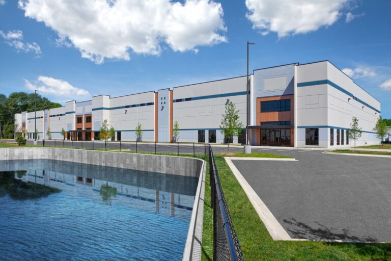 A modern industrial building with a blue sky and a pond in the foreground.